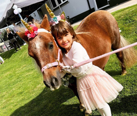 A young person posing with unicron pony, they both have unicorn horns on!
